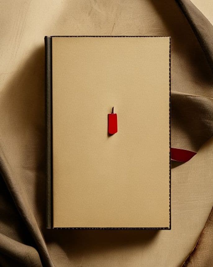 A leather-bound notebook resting on warm paper, with a red bookmark ribbon.
